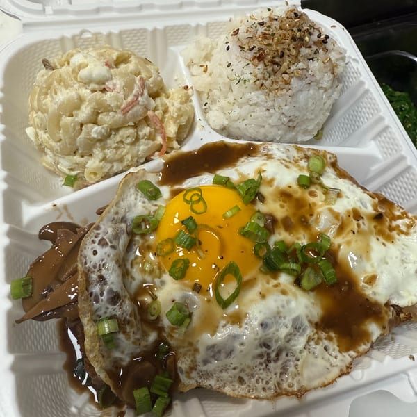 Kanaka's Loco Moco with a fried egg, gravy, rice, and macaroni salad in a takeout container.