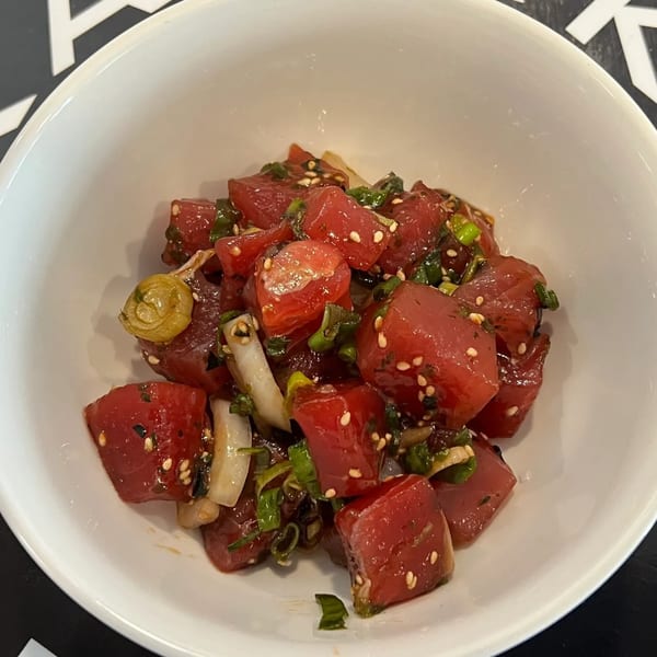 A white bowl filled with Kanaka poke, featuring diced red tuna, green onions, and sesame seeds.