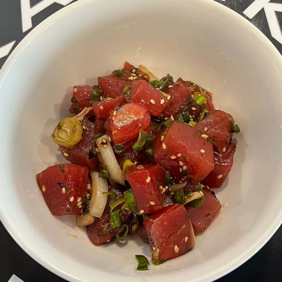 A white bowl filled with Kanaka poke, featuring diced red tuna, green onions, and sesame seeds.