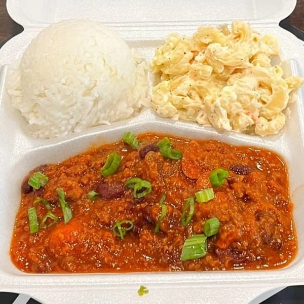 A takeout container with chili, white rice, and macaroni salad, garnished with green onions.