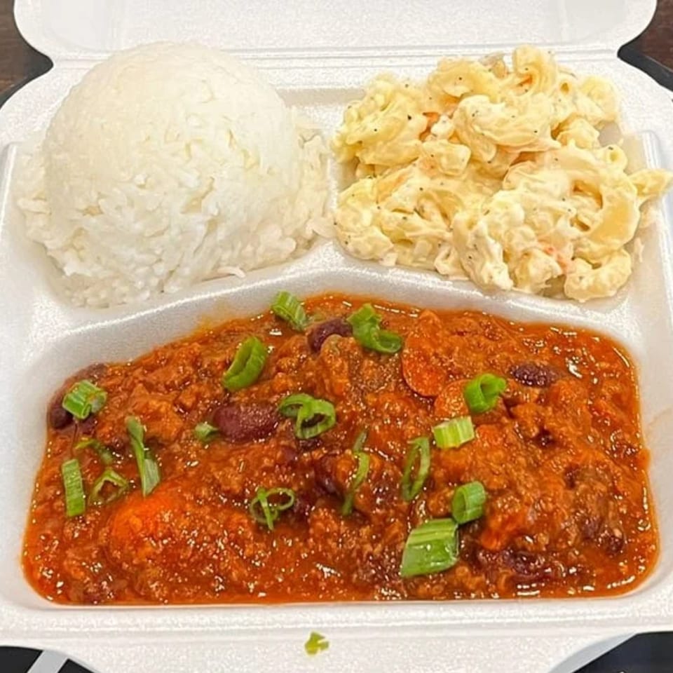 A takeout container with chili, white rice, and macaroni salad, garnished with green onions.