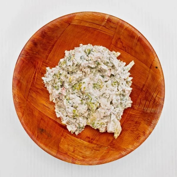 Creamy poke with green herbs and spices in a wooden bowl on a white surface.