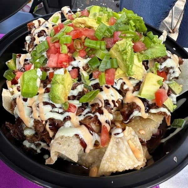 Kanaka poke nachos with meat, avocado, tomatoes, green onions, and two sauces in a black bowl.