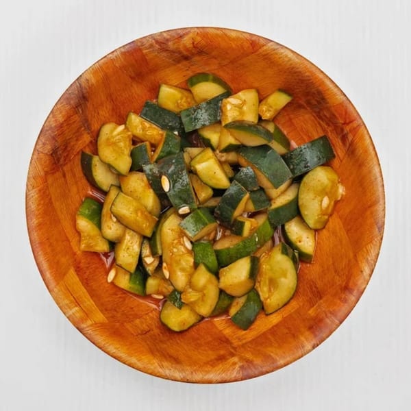 Top-down view of a wooden bowl filled with seasoned, chopped cucumbers.