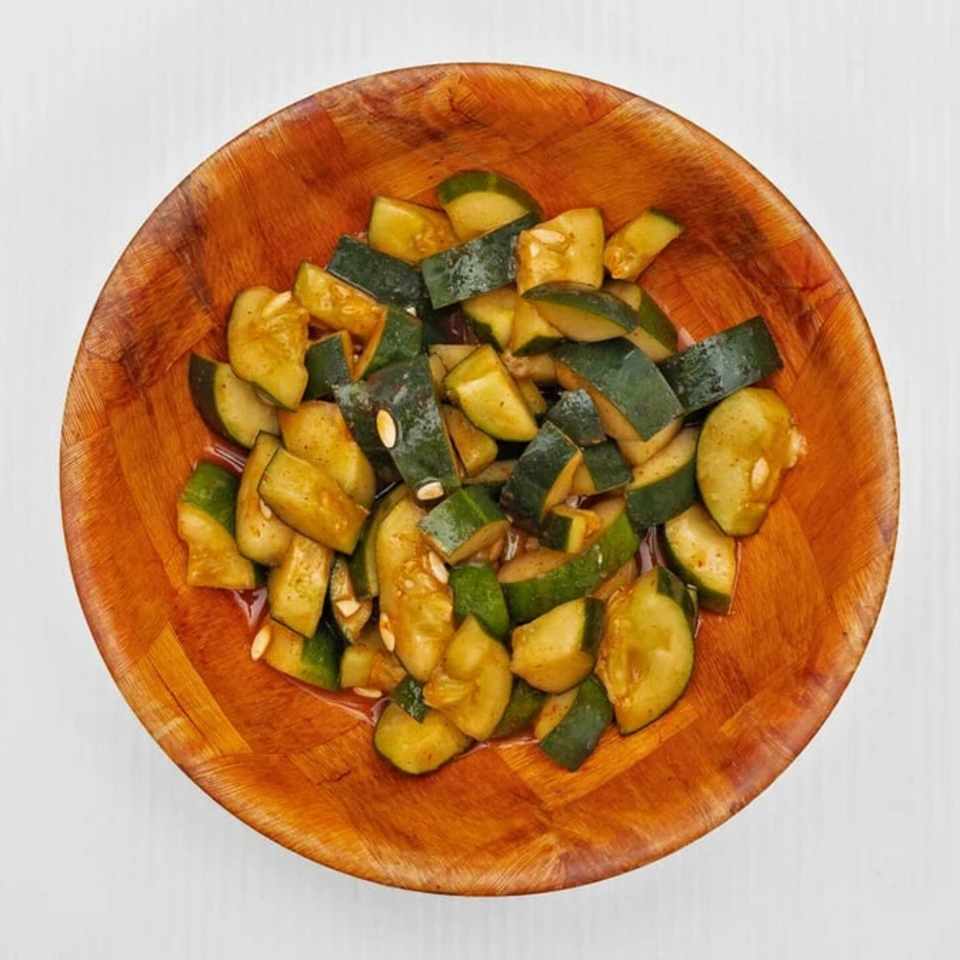 Top-down view of a wooden bowl filled with seasoned, chopped cucumbers.