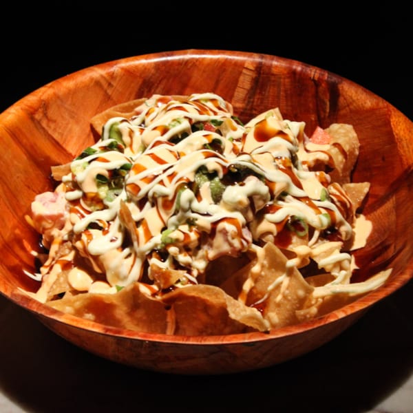 Kanaka poke nachos, drizzled with white and brown sauces, in a rustic wooden bowl.
