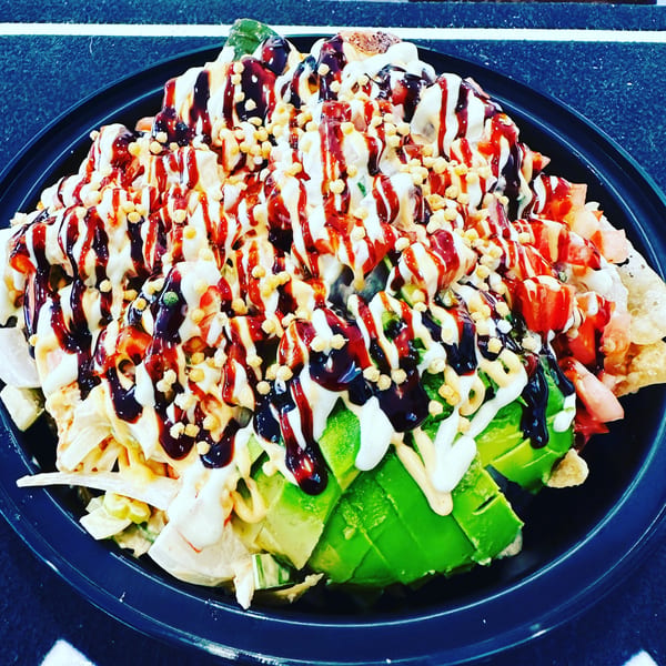 Kanaka poke bowl with avocado, various toppings, and drizzled sauces in a black bowl.