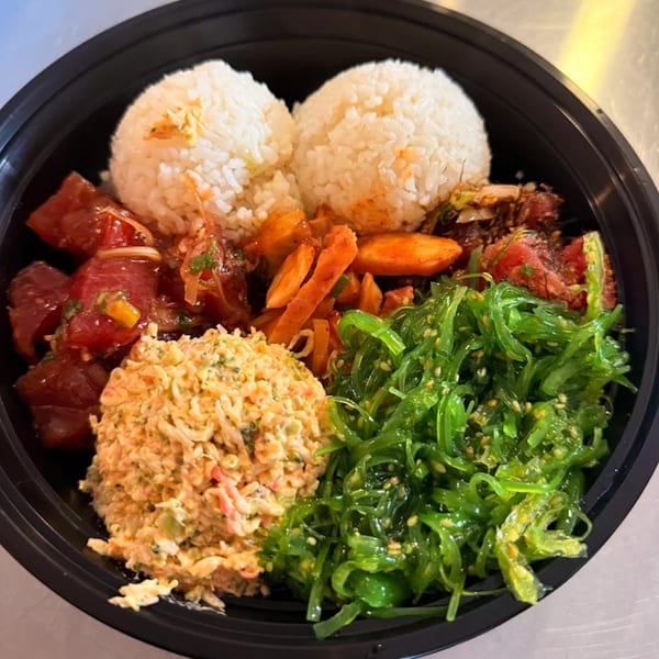 A Kanaka poke bowl with tuna, crab salad, seaweed, and rice in a black bowl.
