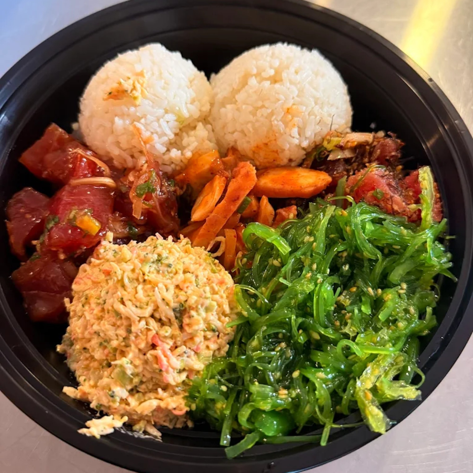 A Kanaka poke bowl with tuna, crab salad, seaweed, and rice in a black bowl.