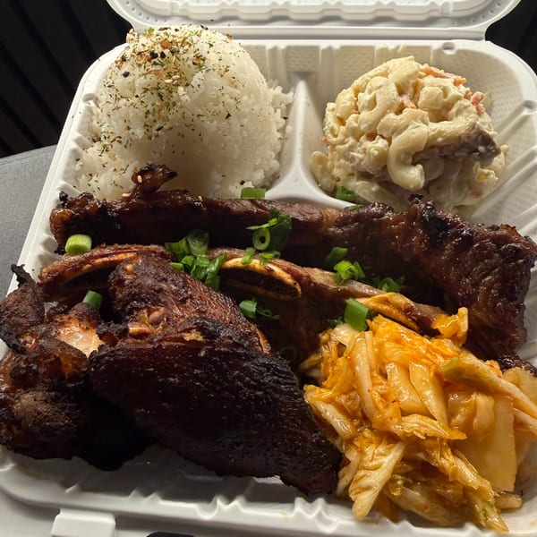 Kanaka's poke plate with grilled ribs, rice, macaroni salad, and kimchi in a takeout container.